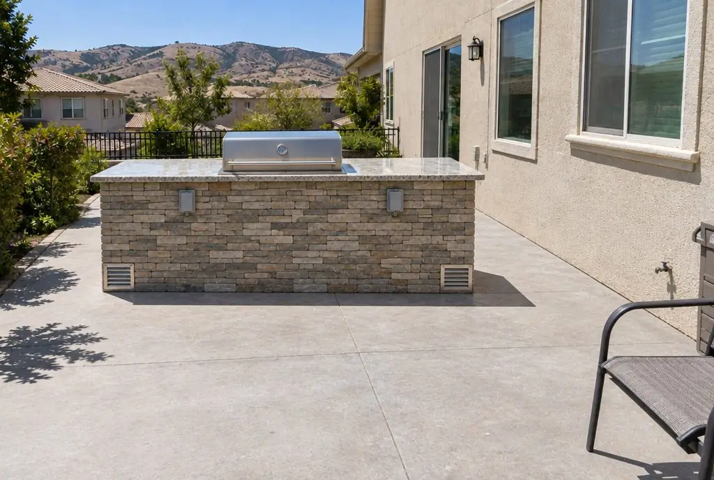 Illustration: the same patio with a finished stone-clad island, a built-in grill, GFCI outlets with in-use covers and vent openings in the island face